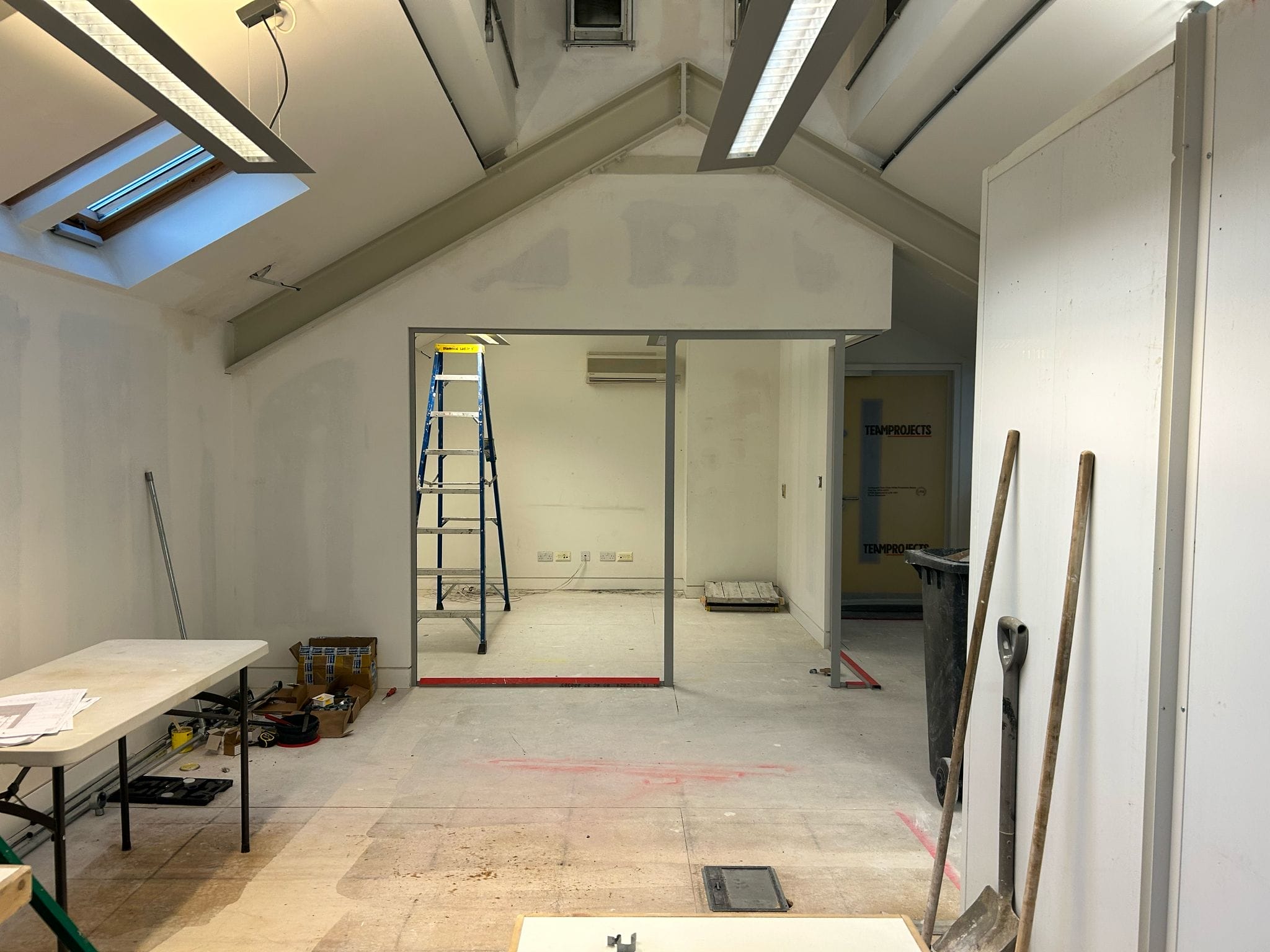 The mezzanine level of the building. a new room has been built. There is space for a glass wall to be set into the room. There is construction equipment throughout the space.